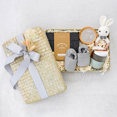 Baby and me gift box includes: Moments of Love: Newborn Milestone Cards by Compendium, Intention Candle Tin, Crochet Bunny Rattle, Light Grey Textured Moccasins, Green Gold Tea Jar