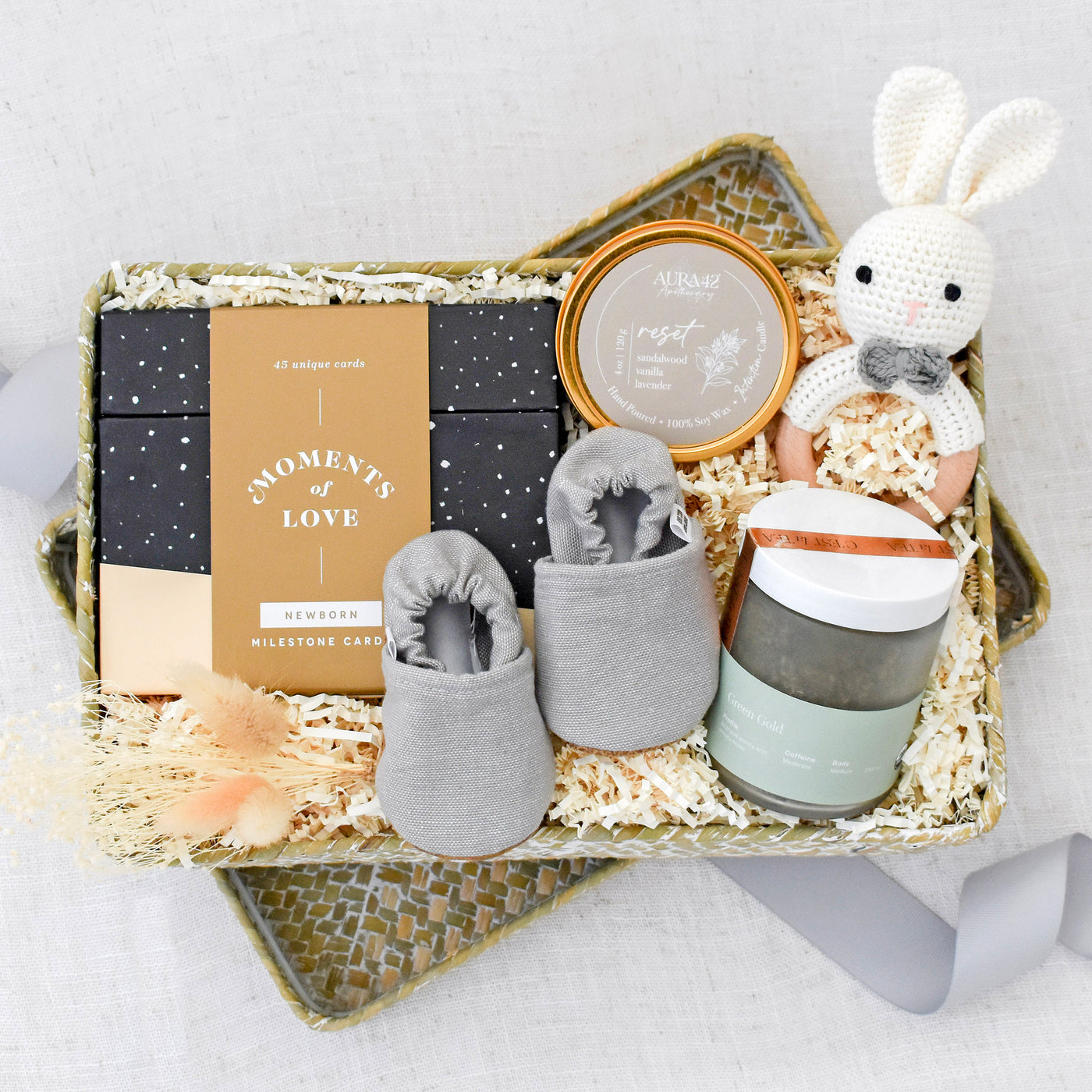 Baby and me gift box includes: Moments of Love: Newborn Milestone Cards by Compendium, Intention Candle Tin, Crochet Bunny Rattle, Light Grey Textured Moccasins, Green Gold Tea Jar